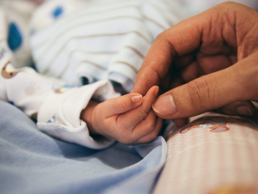 a mom holding her baby's hand in bed