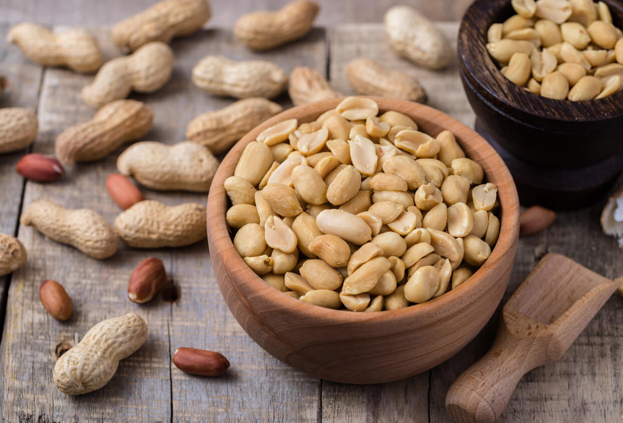 Peanuts in small wooden bowl on natural rustic desk.