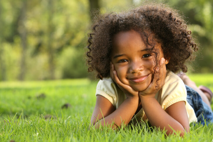 a cute young girl lying in a grass field