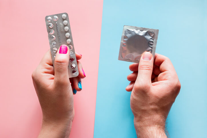 Woman holds birth control pills, man holds condom