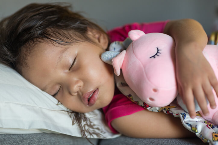 Cute sleeping little asian girl toddler in bed while hugging a stuffed toy