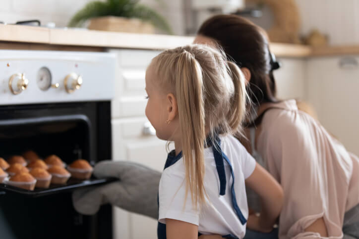 xcited little girl take ready muffins from oven