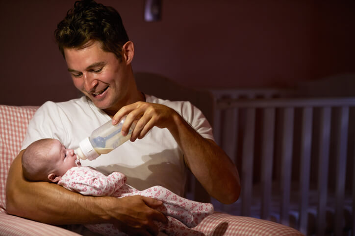 Father Feeding Baby With Bottle In Nursery