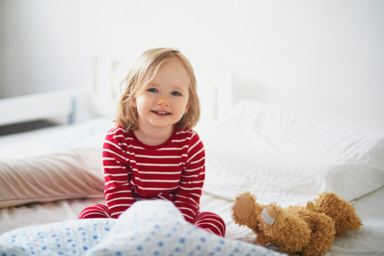 Happy toddler girl in striped red and white pajamas sitting on bed