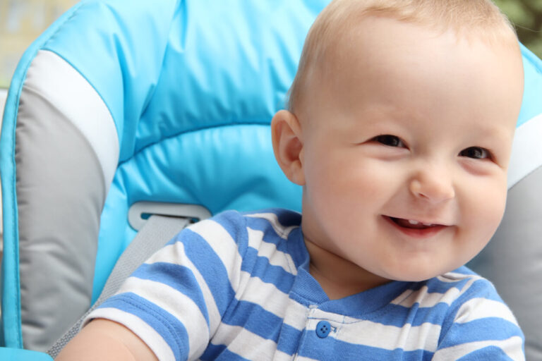 Baby boy sitting in highchair showing his teeth