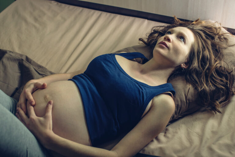 Pregnant woman feeling pain in her belly lying in bed with insomnia at night. Concept of pregnancy and health