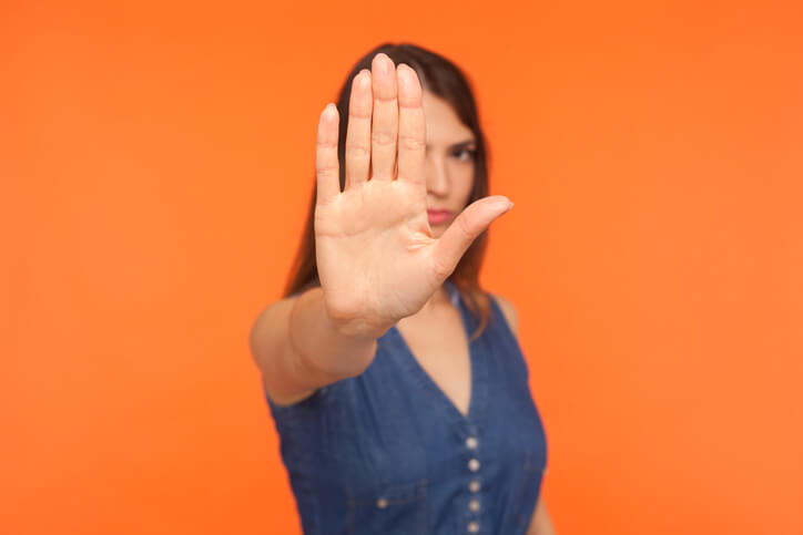 Strict brunette girl with serious bossy expression raising hand and showing stop