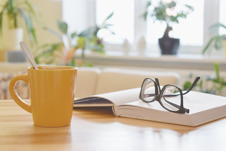 Yellow cup of tea, book and glasses on the table, cozy home interior background