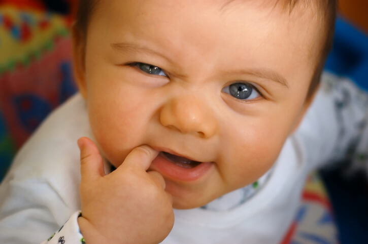 A baby in crib and pajamas teething on finger