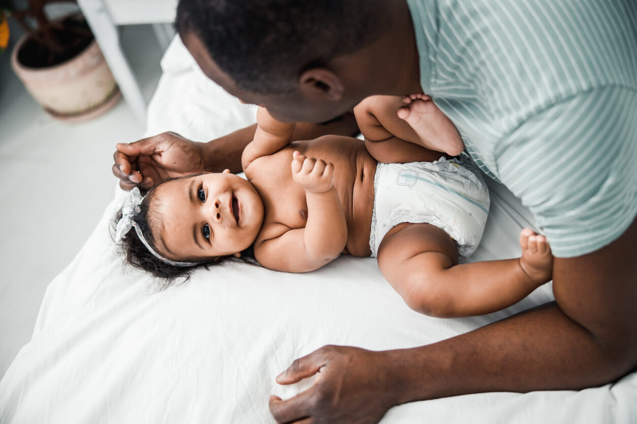 Adorable Afro American baby lying on bed with daddy