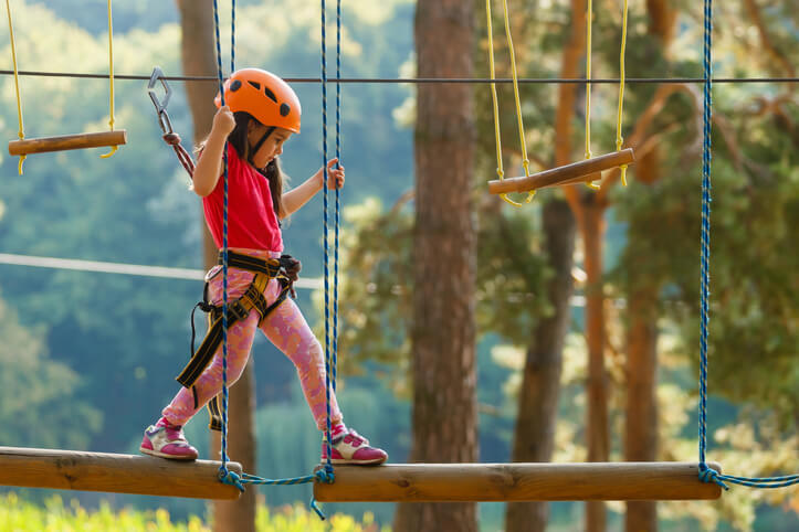 Portrait of cute little girl walk on a rope bridge in an adventure rope park