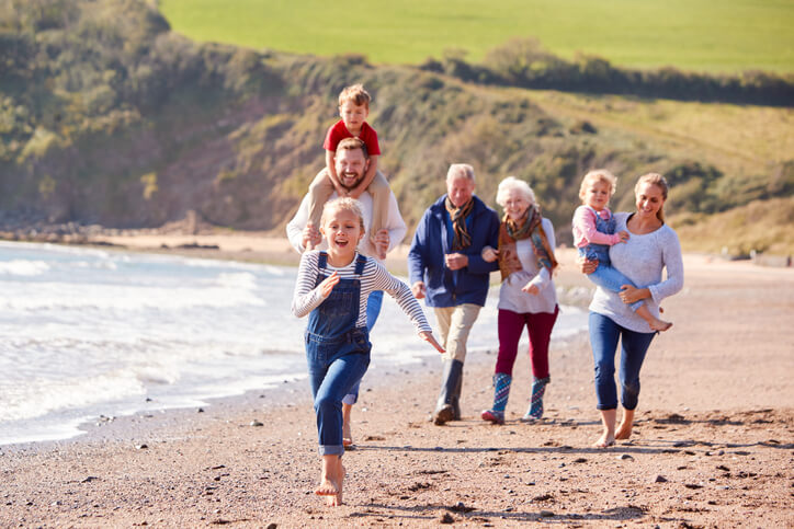 Multi-Generation Family Walking Along Shoreline Of Beach By Waves Together