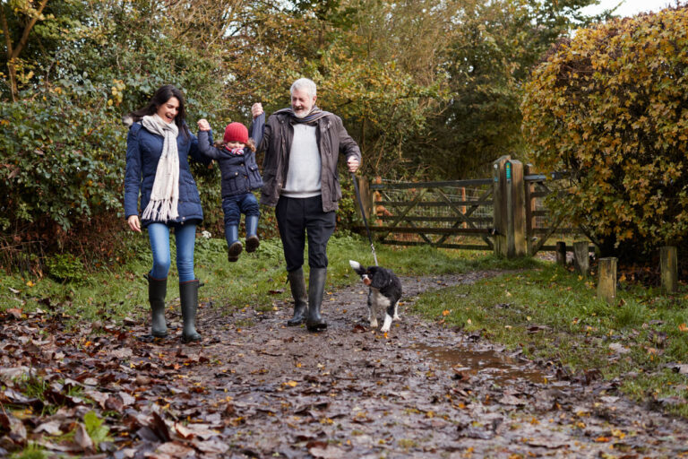 Multi Generation Family Take Dog For Walk In Fall Landscape