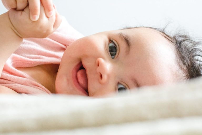 baby smiling while laying on a bed