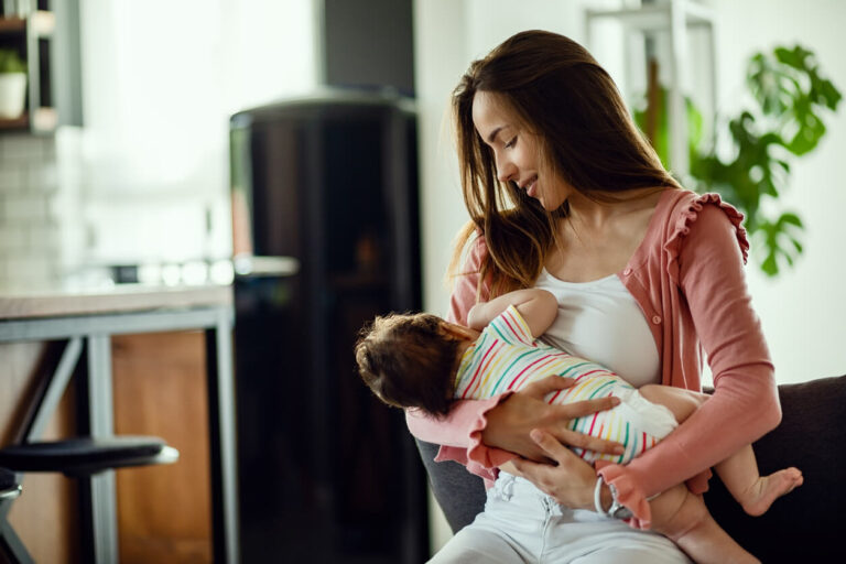 Young smiling mother breastfeeding her baby at home