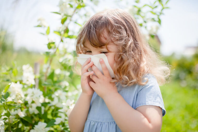 Little girl is blowing her nose near blooming tree