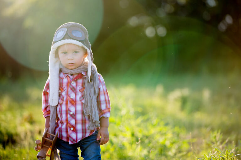 Sweet toddler baby boy, child playing with airplane in poppy fiead, beautiful sunset