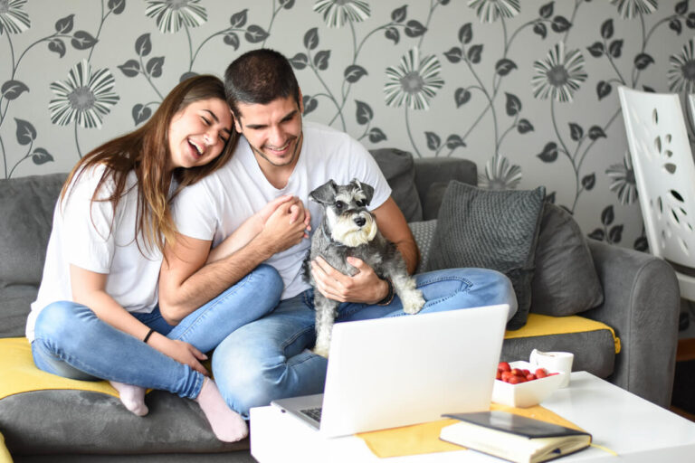 Cheery young couple having video call with friend on laptop computer at home