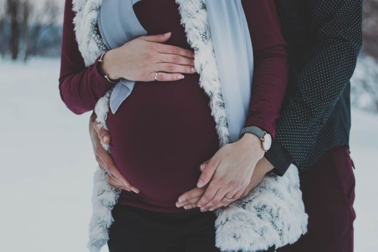 a pregnant mom being held by her partner in the December snow